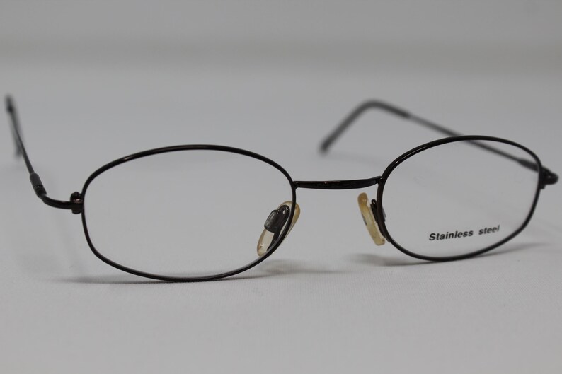 May include: Black oval-shaped eyeglasses with a thin metal frame and clear lenses. The frame is labeled "Stainless steel".