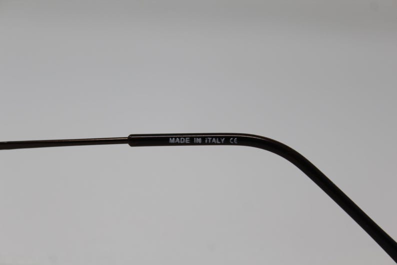 May include: Close-up of the arm of a pair of black eyeglasses with the text "MADE IN ITALY CE" printed on the arm.