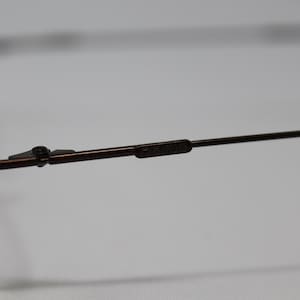 May include: Close-up of the brown metal frame of a pair of eyeglasses. The frame has a spring hinge and the brand name "Calvin Klein" is visible on the arm.