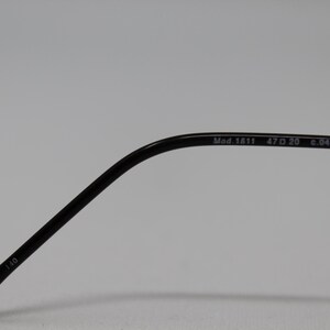May include: Close-up of the arm of a pair of black eyeglasses. The arm is marked with the text "Mod. 1611 47□20 c.04 130 39 110".