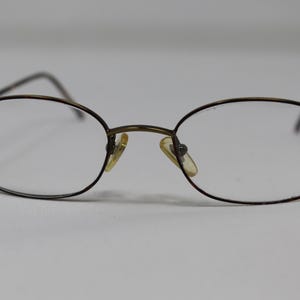 Puede incluir: Un par de gafas ovaladas con montura de metal marrón y lentes transparentes.