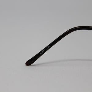 May include: Close-up of the arm of a pair of black eyeglasses with the text "48D 21 140" printed on the arm.