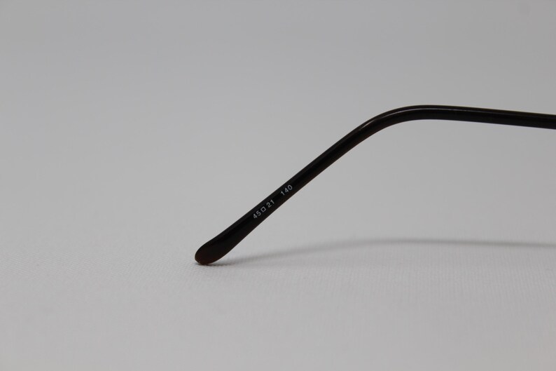 May include: Close-up of the arm of a pair of black eyeglasses with the text "48D 21 140" printed on the arm.