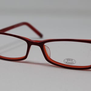 May include: Red plastic framed eyeglasses with clear lenses. The brand name "STEVE MADDEN" is printed on the right lens.
