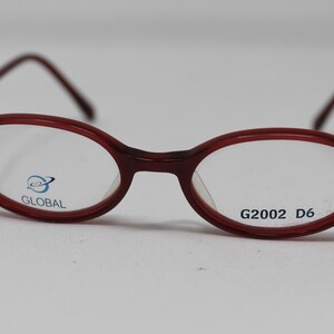 Puede incluir: Gafas ovaladas de color rojo con lentes transparentes. Las monturas tienen la palabra "GLOBAL" impresa en la lente izquierda y "G2002 D6" impresa en la lente derecha.