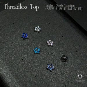 May include: An assortment of threadless tops in a flower design. The tops are made of implant grade titanium and come in various colors, including blue, silver, and black. The text "Threadless Top" and "Implant Grade Titanium" are visible.