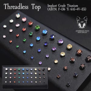 May include: A collection of threadless tops made of implant grade titanium (ASTM F-136 Ti 6Al-4V-Eli). The jewelry pieces feature round, faceted gemstones in various colors including clear, pink, green, blue, purple, yellow, and brown.