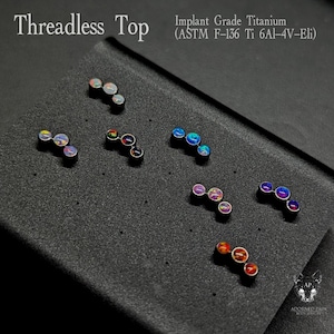 Könnte beinhalten: Eine Auswahl an Gewindespitzenteilen, jeweils mit drei bunten, schillernden Edelsteinen in einer gebogenen Reihe. Die Schmuckstücke sind auf einer dunkelgrauen Oberfläche präsentiert. Der Text "Threadless Top" und "Implant Grade Titanium" ist sichtbar.