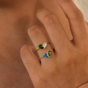 May include: A gold ring with three teardrop-shaped gemstones. The gemstones are green, blue, and clear.