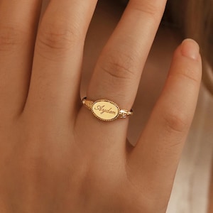 Könnte beinhalten: Ein goldener Siegelring mit ovaler Oberfläche. Der Ring trägt den Namen "Aydan" in zarter Schrift eingraviert. Das Band hat ein strukturiertes Design. Der Ring wird am Finger getragen.
