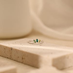 K&ouml;nnte beinhalten: Ein Silberring mit drei im Marquise-Schliff geschliffenen Edelsteinen, die wie ein Blatt angeordnet sind. Der mittlere Stein ist tief smaragdgr&uuml;n und wird von zwei kleineren, helleren lindgr&uuml;nen Steinen flankiert.