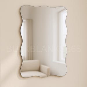 May include: A wavy-edged mirror hangs on a beige wall. The mirror reflects a room with a white armchair, a window, and a curtain. The mirror's frame is thin and dark, and the overall design is modern and minimalist.