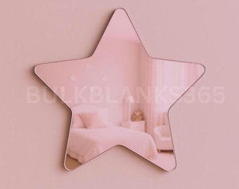 May include: A pink star-shaped mirror mounted on a pink wall. The mirror reflects a bedroom scene with a bed, nightstand, and chair. The text "BULKBLANKS365" is visible on the mirror's surface.