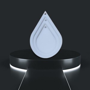 May include: Three white teardrop-shaped cookie cutters of different sizes, stacked on top of each other, on a black pedestal.