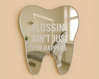 May include: A tooth-shaped mirror with the text "FLOSSIN' AIN'T JUST FOR RAPPERS" etched on the surface. The mirror reflects a dental office setting. The mirror is silver and hangs against a beige wall.