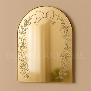 May include: A gold-colored arched mirror with a bow at the top and floral vine detailing. The mirror has a smooth, reflective surface and is framed by etched roses and leaves. The overall design is elegant and decorative.
