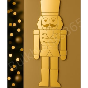 May include: A golden-colored, stylized nutcracker figure with a tall hat, mustache, and uniform. The design is a flat illustration, suitable for holiday decor. The background is a warm, neutral tone, with a blurred Christmas tree on the left.