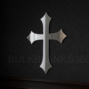 May include: A silver-colored cross with pointed ends is mounted on a black wall. The cross is the focal point, with a simple, elegant design. The text "BULKBLANKS365" is visible on the wall.