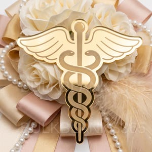 May include: A gold-colored medical caduceus emblem with wings and intertwined snakes, set against a backdrop of cream-colored roses, ribbons, pearls, and feathers. The emblem is the focal point, symbolizing healthcare.