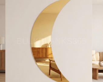 May include: A crescent moon-shaped mirror with a gold finish is mounted on a white wall. The mirror reflects a room with wooden furniture and a chair. The text "BULK TANKS365" is visible on the wall.