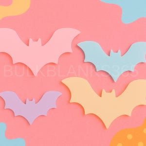 May include: Four pastel-colored bat shapes in pink, blue, lavender, and yellow are arranged on a pink background with abstract shapes. The bats are symmetrical with pointed wings and a small head. The text "BULKBLANKS365" is visible.