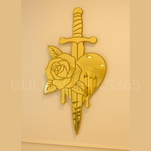 May include: A gold-colored wall art piece featuring a sword piercing a heart, with a rose and leaves. The design is a mirror-like finish, mounted on a light-colored wall. The text "BULK XS365" is visible.