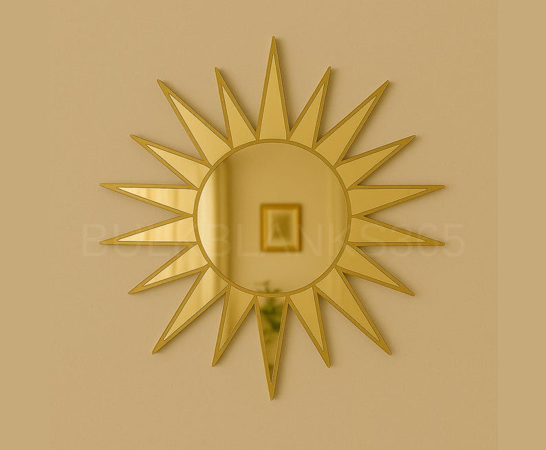 May include: A gold-colored sunburst mirror with a circular center and pointed rays. The mirror is mounted on a light-colored wall. The mirror reflects a room with a framed picture.