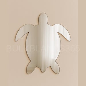 May include: A silver-colored turtle-shaped wall mirror. The mirror is mounted on a beige wall. The mirror's design includes a head, four flippers, and a rounded shell. The text "BULKBLANKS365" is visible in the lower left corner.
