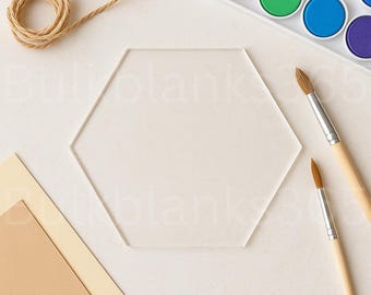 May include: A clear, hexagonal acrylic blank sits on a white surface, surrounded by art supplies. A roll of twine, two paintbrushes, a watercolor paint set with pink, green, blue, and purple paints, and two pieces of paper are also visible.