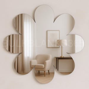 May include: A flower-shaped wall mirror with a petal design. The mirror reflects a room with a beige armchair, a framed picture, a table, and a lamp. The mirror is mounted on a white wall.