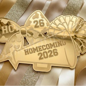 May include: A gold-colored Homecoming 2026 keepsake with a bow, megaphone, and pom-pom design. The bow features the letters "HC" and the number "26". The megaphone displays "HOMECOMING 2026".