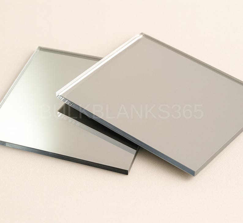 Puede incluir: Dos azulejos de espejo de vidrio cuadrados con superficies lisas y reflectantes y bordes rectos y limpios. El texto BULKBLANKS365 est&aacute; impreso en una fuente clara y semitransparente en el centro de las superficies de espejo superpuestas.