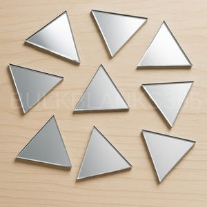 May include: Nine mirrored glass triangles arranged on a light wood surface. Each triangle has a reflective surface and a black border. The triangles are evenly spaced, creating a geometric pattern.