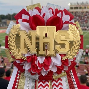 May include: A decorative mum with red, white, and gold accents. The mum features a gold-colored emblem with the letters "NHS" and is surrounded by a laurel wreath. Ribbons and embellishments in red, white, and gold complete the design.