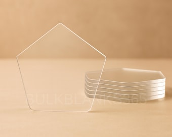 May include: Clear, pentagon-shaped acrylic blanks. One blank stands upright, with a stack of similar blanks beside it. The blanks are transparent and appear to be made of a smooth, polished material. The background is a solid, neutral color.