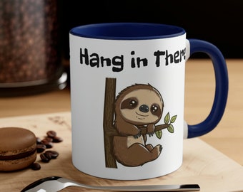 May include: White ceramic coffee mug with a blue rim and handle. The mug features a cartoon sloth hanging from a branch with the text "Hang in There" printed on the front.