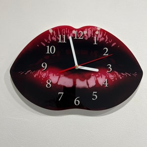 Könnte beinhalten: Eine rote und schwarze lippenförmige Uhr mit weißen Zahlen und Zeigern. Das Zifferblatt der Uhr hat eine glänzende Oberfläche.