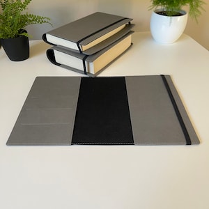 May include: A gray book cover with a black elastic band and a black fabric interior. The cover has three pockets on the left side.