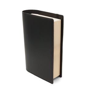 Puede incluir: Una cubierta de libro de cuero negro con un libro liso de color marrón claro en el interior.