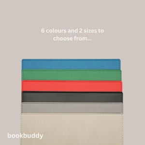 May include: Six bookends in different colors, including blue, green, red, black, gray, and beige. The bookends are stacked on top of each other. The text "bookbuddy" is at the bottom of the image. The text "6 colours and 2 sizes to choose from..." is at the top of the image.