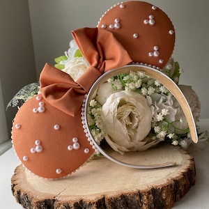May include: A pair of brown mouse ears with a white headband. The ears are decorated with white pearl-like beads.