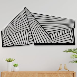 以下が含まれることがあります： モダンなデザインの黒い幾何学的なウォールアート。アートは金属製で、黒い仕上げになっています。白い壁に、木製のコンソールテーブルの上に飾られています。