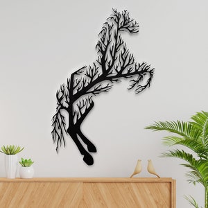 May include: Black metal wall art depicting a horse silhouette made of branches. The art is mounted on a white wall with a wooden cabinet and potted plants below.