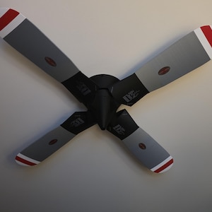 May include: A ceiling fan featuring four blades designed to resemble airplane propellers. The blades are primarily grey with black bases and red and white striped tips. A central black motor housing connects the four blades in an X-shape.