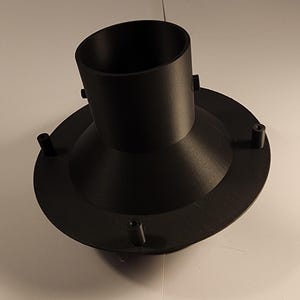 以下が含まれることがあります： 円筒形の上面と幅広の円形基部を備えた、黒いプラスチック製の漏斗型オブジェクト。基部には、縁に沿って均等に配置された4つの小さな円筒形の突起があります。このオブジェクトは、流れを誘導するように設計されています。