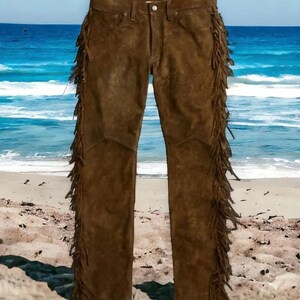 May include: Brown suede pants with fringe detailing along the sides. The pants are photographed against a beach background.