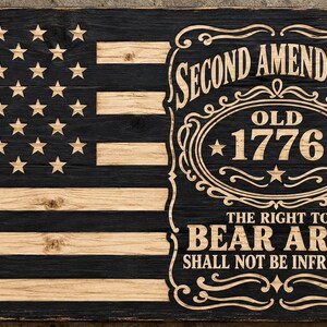 May include: A rectangular wooden sign featuring a stylized American flag with alternating black and natural wood stripes and stars. The right side displays engraved text reading Second Amendment, Old 1776, The Right To Bear Arms Shall Not Be Infringed.
