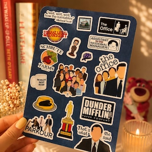 May include: A dark blue sticker sheet featuring various designs inspired by The Office, including the Dunder Mifflin logo, a Dundie award, a World's Best Boss mug, Schrute Farms, and quotes like Well, well, well, how the turntables and That's what she said.