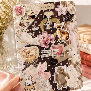 May include: A rectangular collage card featuring a dark brown background with white polka dots, decorated with various stickers including a fawn, a swan, Snoopy, two rabbits, a butterfly, pink flowers, a martini glass, and text reading p.s. i love u and dream a little dream of me.