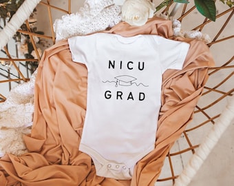 May include: White baby onesie with black text that reads "NICU GRAD" with a graduation cap graphic above the word "GRAD".